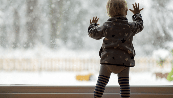 Toddler In Window Snowing Outside 1
