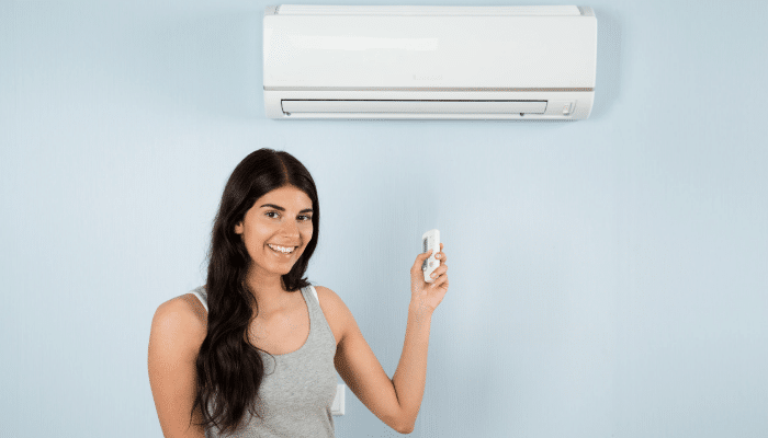 Woman Holding Remote Control In Front Of Air Conditioner 1